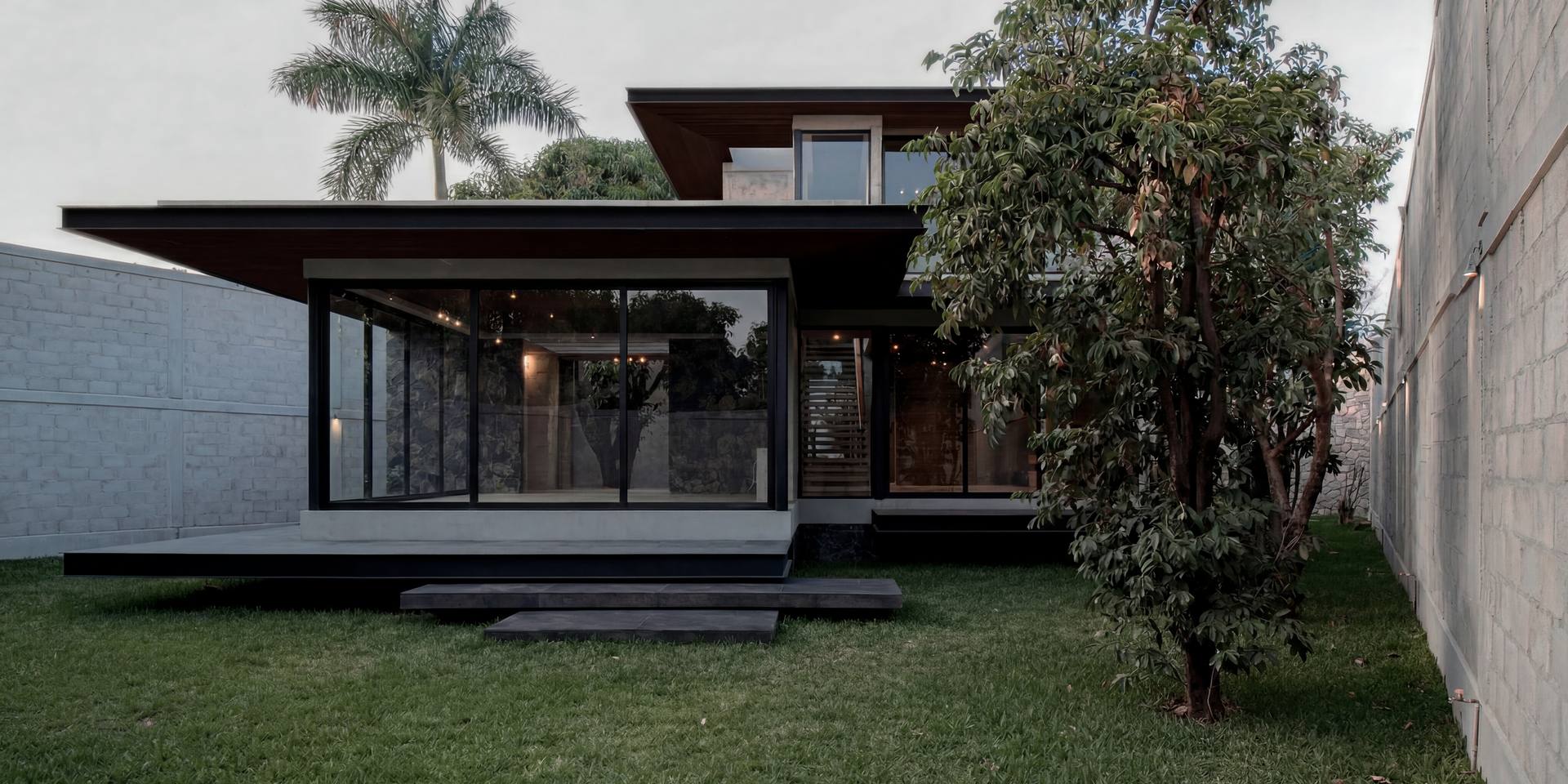Casa de planta baja con grandes ventanales, terraza de acero y un árbol al frente