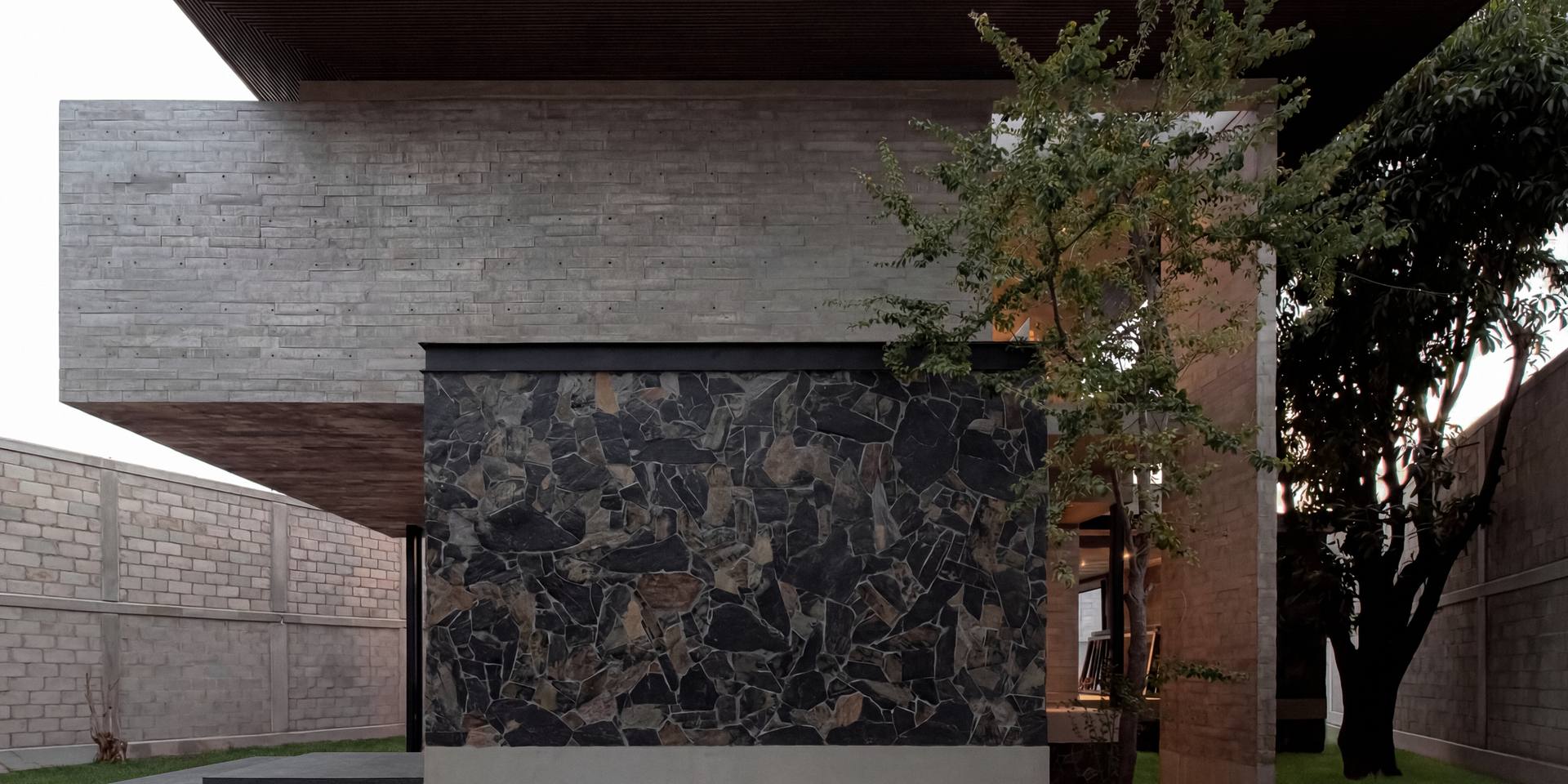 Volumen de concreto aparente con muro de piedra volcánica y losa de madera