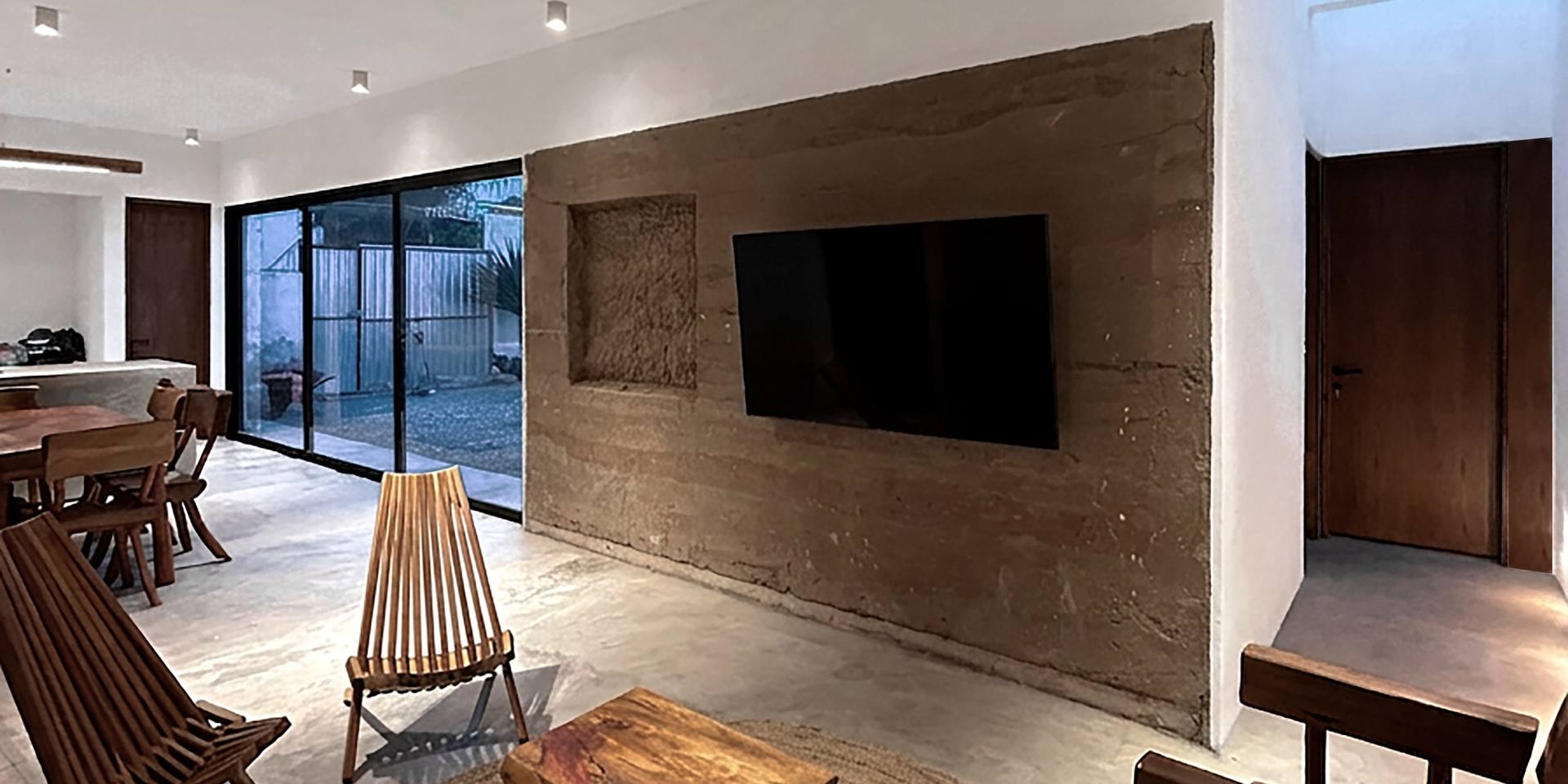 Sala con muro de tierra apisonada, mobiliario de madera y tapete de fibra natural